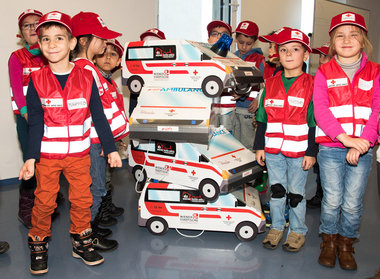Eine Gruppe Kindergartenkinder posiert mit Rotkreuzwesten und einigen Rettungsautos aus Karton