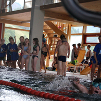 Ein Bursche schwimmt in der Freistilstaffel und wird von anderen Kindern im Hintergrund angefeuert