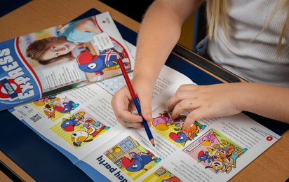 © ÖJRK/Gianmaria Gava Kind das mit Buntstift etwas in einer Mehr als Lesen Zeitschrift unterstreicht.