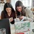 Zwei junge Frauen sitzen nebeneinander und schauen konzentriert auf ihr Handy. Eine der beiden hält eine Google-Cardboardbrille in der Hand. Vor ihnen steht eine #humanity-Zivilcourage und Werte-Box des Jugendrotkreuzes.