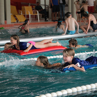 Blick auf zwei Schwimmbahnen auf denen zwei Kinder ziehen bzw. schieben ein Kind auf einer Luftmatratze im Rahmen der Rettungsstaffel beim Pinguin Cup 2023