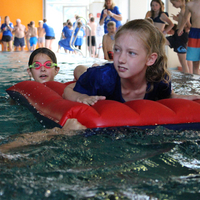 Zwei Kinder ziehen bzw. schieben ein Kind auf einer Luftmatratze im Rahmen der Rettungsstaffel beim Pinguin Cup 2023
