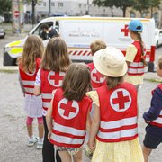 Kinder in roten Warnwesten schauen sich ein Rettungsauto an.
