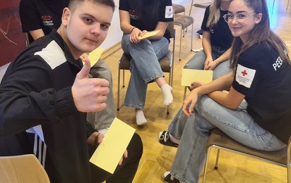 5 Jugendliche sitzen im Kreis und lächeln in die Kamera. Einer von ihnen zeigt seinen Daumen hoch.