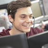 Ein Mitarbeiter des Service-Centers der Blutspendezentrale sitzt mit Headset vor zwei Monitoren und lächelt
