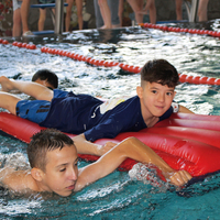 Zwei Kinder davon eines auf einer Luftmatratze schwimmen bei einer Rettungsstaffel im Rahmen des Pinguin Cups 2023