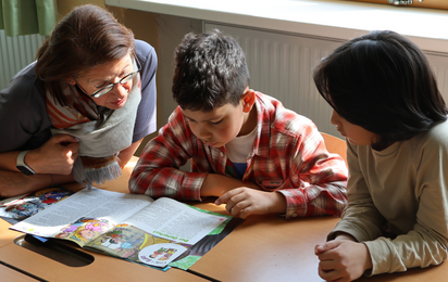 Eine Lesepatin liest mit Kindern aus einer Zeitschrift