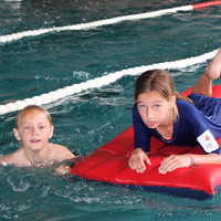 Zwei Kinder davon eines auf einer Luftmatratze schwimmen bei einer Rettungsstaffel im Rahmen des Pinguin Cups 2023