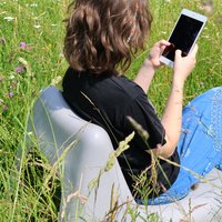 Eine Jugendliche sitzt in der Wiese auf einem weißen Plastikstuhl und übt auf einem Tablet, wie WhatsApp-Beratungen richtig durchgeführt werden.