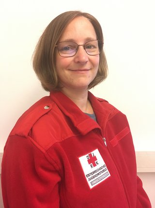 Frau mit schulterlangen braunen Haaren und Brille in Rot-Kreuz Jacke lächelt direkt in die Kamera