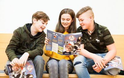 Zwei Burschen lesen bei einem Mädchen begeistert mit.