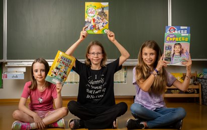 © ÖJRK/Gianmaria Gava Drei Kinder, die Mehr als Lesen Zeitschriften hochhalten.