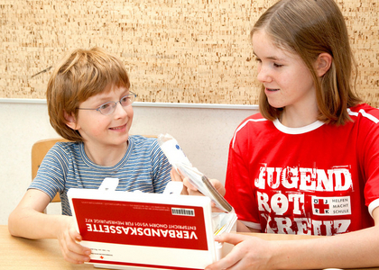 Zwei Kinder mit Verbandskassette und Jugendrotkreuz-T-Shirts